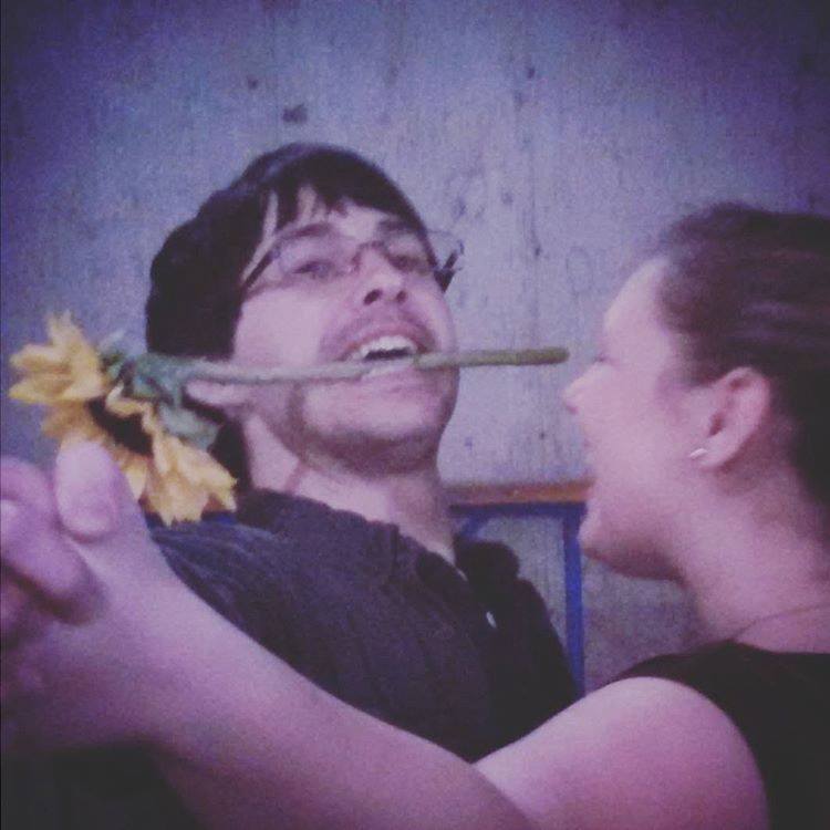 Brian with a cut sunflower held by the stem in his teeth. He is doing a mock Tango dance with his wife.